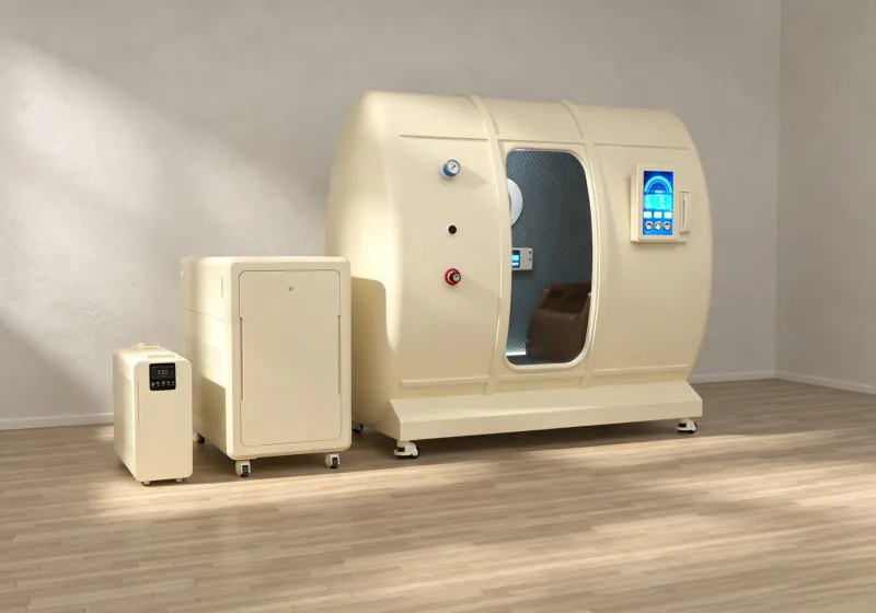 Angled view of a cream seated hyperbaric chamber with a brown seat, pressure gauge and two external equipment units.