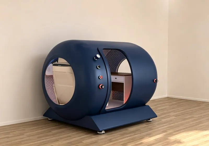 Blue hard shell hyperbaric chamber with a circular side window, cream seat, interior desk and pressure gauge.