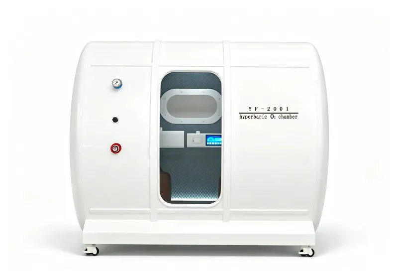 White hard shell hyperbaric chamber with a transparent door, oval viewing window, padded interior and pressure gauge.